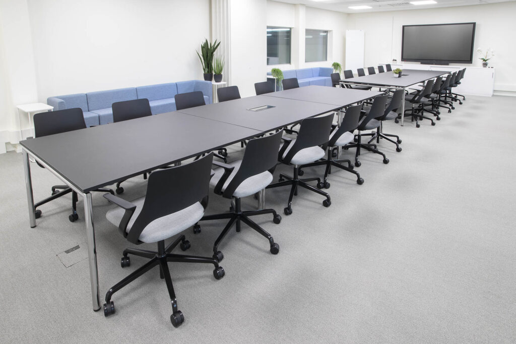 Meeting room with 24 seats, big screen on the wall (and another on the other side not visible)
Two sofas on the side and two windows.