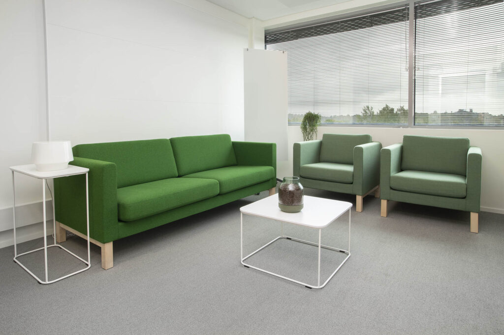 Ikkunallinen huone, jossa on sohva ja kaksi nojatuolia sekä kaksi pöytää. Valkotaulu.