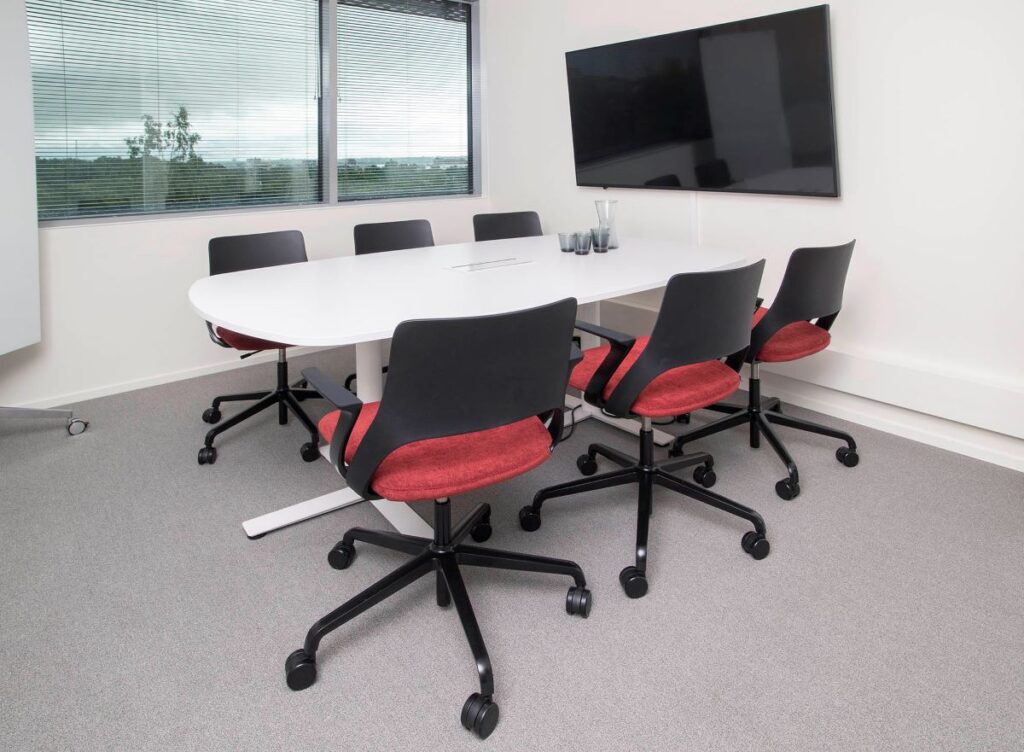 Ikkunallinen huone, jossa on iso näyttö ja pöydän ympärillä kuusi tuolia. Valkotaulu.