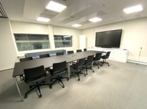 Meeting room with a table and 12 seats, a screen and windows on the wall